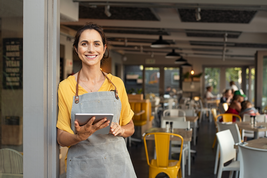 business owner olds tablet and leans against open door frame into restaurant