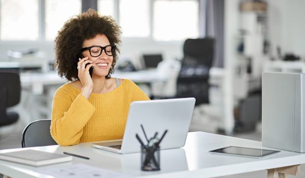 Charming mixed race woman talking on the phone and using a laptop to create eye-catching graphics.